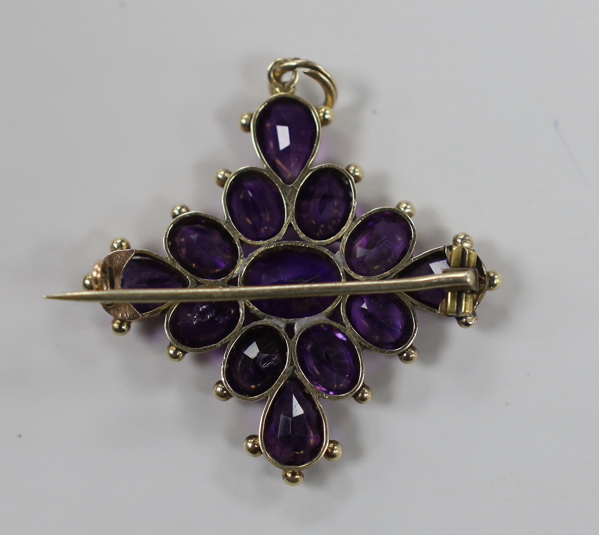 An early 20th century yellow metal and amethyst cluster set quatrefoil pendant brooch, 42mm, gross weight 7.5 grams.